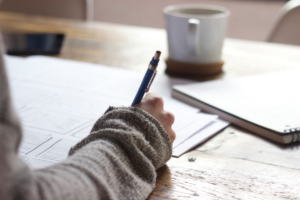 person writing on brown wooden table near white ceramic mug — Foto por Unseen Studio na Unsplash